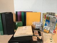 Wide shot of the movie script, postage stamps, binder folders, hanging labels, hole reinforcements, scantron sheets, notebooks, and various office supplies on flat surface