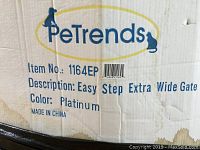 Close-up of the cardboard packaging label showing brand, model number, color, and description of the pet gate.