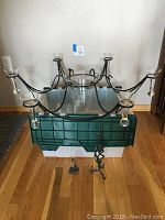 Front angle showing full chandelier with six arms and central glass vase, green tote beneath.