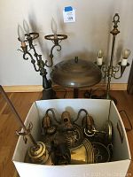 Three brass lamps placed on the floor and a cardboard box filled with various brass lamp parts including arms and shades.