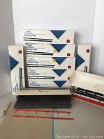 Multiple boxes of VeloBinder Binding Strips and the VeloBinder machine laid on a table, with some loose red binding strips in front