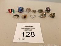 Lot of 11 various rings including lucite, glass, and sterling silver on a table.