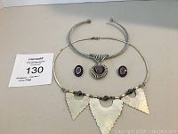 Full set showing necklace with three large hammered metal arrowhead-shaped pendants, matching earrings with purple oval stones, and silver twisted metal choker with fan-shaped centerpiece and purple stone.