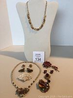 Full lot view showing two necklaces on and in front of a jewelry bust, four pins and three pairs of earrings arranged in front.