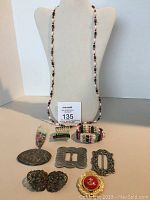 Full display of lot showing marcasite buckle/pin, glass pendant, hematite bead strands, and assorted pins on display stands.