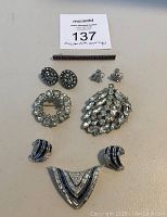 Full lot of jewelry laid flat: one pendant/slide, three pins, and three pairs of earrings.