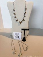 Full view of three necklaces displayed on stands and pair of earrings on earring stand