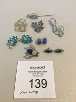 Top view photo of all pins and earrings on a white surface with auction tag.