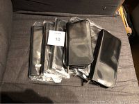 Seven black zippered cases lying on fabric surface, some still in packaging, with MAC label visible