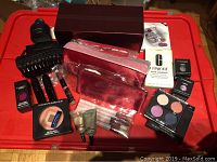 Overview of the lot showing makeup items, cosmetic bags, brushes, and hair clip on red surface.