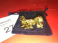 Gold plated Estee Lauder charm bracelet with frog charm inside black velvet pouch, showing green Swarovski eyes, clear crystals on crown, and lobster clasp.