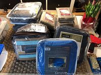 Photo showing assorted packaged furniture slip covers stacked, including brands Sure Fit and Room Essentials with variety in cover types and colors.