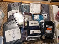 Top-down view of assorted packaged curtain panels, blackout curtains by Sun Zero, pleated shades, and curtain hardware on a bed surface.