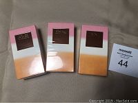 Three boxed Estee Lauder Bronze Goddess shimmering body oil sprays, boxed and sealed, pink to orange gradient design with metallic logo.