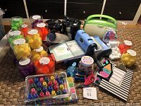 Photo showing the Sizzix Big Kick and Cuttlebug die cutters, jars of multicolored pom poms, rubber stamps, ink pads, paint bottles, and scissors arranged on carpet.