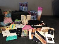 Photo of miscellaneous new beauty and cosmetic products, including boxed Crabtree & Evelyn and Bumble and bumble, sample packets, a black cosmetic case, and a pink disposable slippers pack.