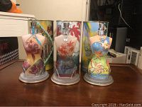 Front view of three female torso-shaped Jean Paul Gaultier bottles, each with distinct floral and tropical designs, placed on a wooden surface.