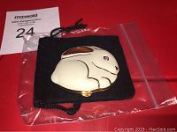 White enameled rabbit-shaped pressed powder compact with pink enameled ear, pink crystal eye, and gold tone back on a black velvet pouch inside a plastic bag