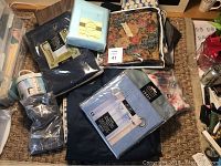 Photo showing assorted packaged and loose linens including curtain panels in navy and light blue, pillowcases, a floral tapestry, and other linen pieces.