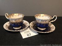 Two Royal Albert bone china cups and matching saucers with deep blue and gold detailing, side view.