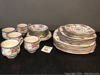 Photo showing 6 floral bone china teacups and stacks of saucers and plates in Royal Albert Petit Point pattern.