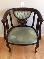 Front view of the antique chair showing tufted fabric seat and back panel inside curved wooden frame.