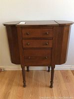 Front view of vintage wooden cabinet with three drawers and drop-leaf sides closed. Surface wear visible.