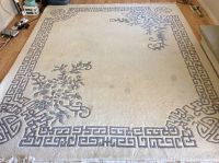 Full view of the large cream and gray area rug with floral and geometric border designs and visible stains.