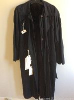 Front view of black raincoat on hanger with tags attached, showing long sleeves, buttons, and belt.
