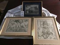 Photo of three framed sketches, two with gold frames 13x17 inches, one with blue matting frame 13x11 inches, displayed on a table.