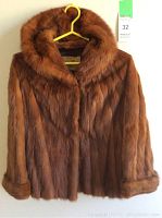 Front view of brown vintage fur coat hung on yellow hanger against light background.