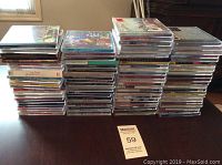 Four stacks of music CDs on a table, showing front covers and spines including multiple artists and genres.