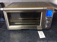 Front view of Breville toaster oven showing stainless steel body, glass door, and control panel with blue digital display.