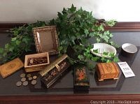 Full lot on table showing all wooden trinket boxes in various shapes and decorations, coins, picture frame, and brass planter with artificial ivy.