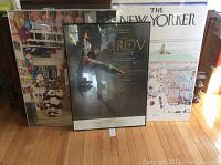 Lot of 3 posters displayed together leaning against a wall on a hardwood floor