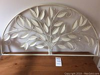 Full view of cream-colored metal wall decor featuring a stylized tree with leaves and curving branches in a semi-circular frame.