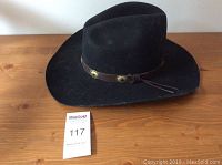 Top down photo of black wool hat with brown leather band and metal conchos.