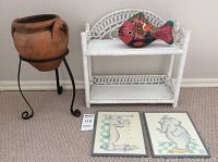 Overall lot showing clay pot on metal stand, wicker shelf, fish figurine and framed prints
