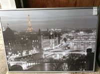 Framed print showing black and white Paris city skyline with Eiffel Tower illuminated, surrounded by silver frame.
