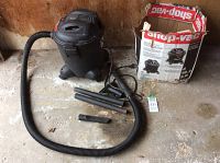 Full view of Shop-Vac wet dry vacuum with flexible hose and multiple black extension tubes on concrete floor, including original box in the background.