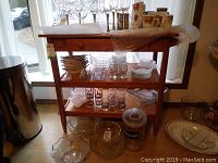 Front view of wooden shelf with drawer, holding glassware and dishes.
