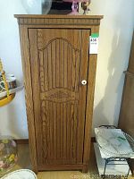 Closed wooden cabinet with single door showing decorative carved panel and white round knob.