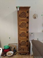 Front view of tall wooden cabinet with four decorative lattice doors and drawer at base.