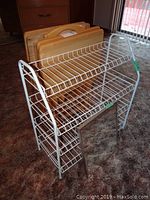 White wire shoe rack with wooden TV tables stacked on top, placed on carpeted floor
