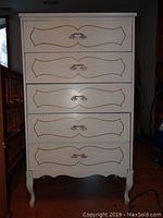 Front view of white French Provincial style 5-drawer lingerie cabinet with gold trim and ornate handles.