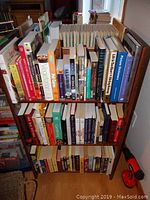 Front view of small wooden bookshelf filled with mixed genre books including cooking and language dictionaries.