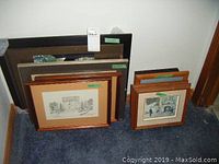 Multiple framed artworks arranged on the floor, various sizes and orientations, visible frames and mats.