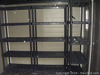 Three sets of black resin shelving units in a shed against the wall, showing overall size and structure.