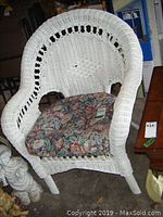 Front view of wicker armchair showing curved arms, decorative open-weave back and floral cushion