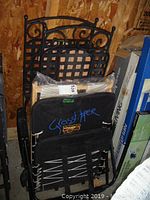 Pair of black metal folding chairs stacked along with the folded beach chair. Decorative metal back design visible.